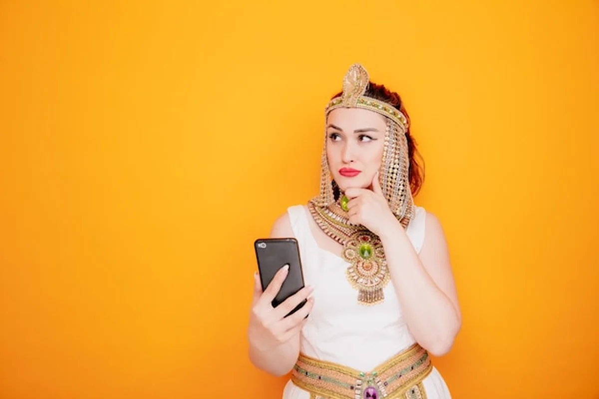 Kobieta jak Kleopatra trzymająca smartfona w egipskim stroju na pomarańczowym tle