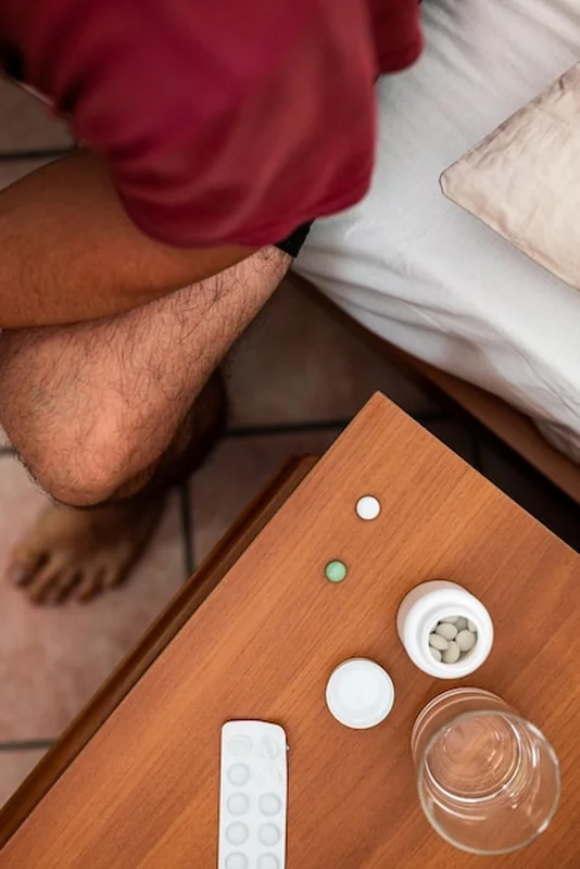 Mężczyzna biorący pigułki na łóżku z wodą