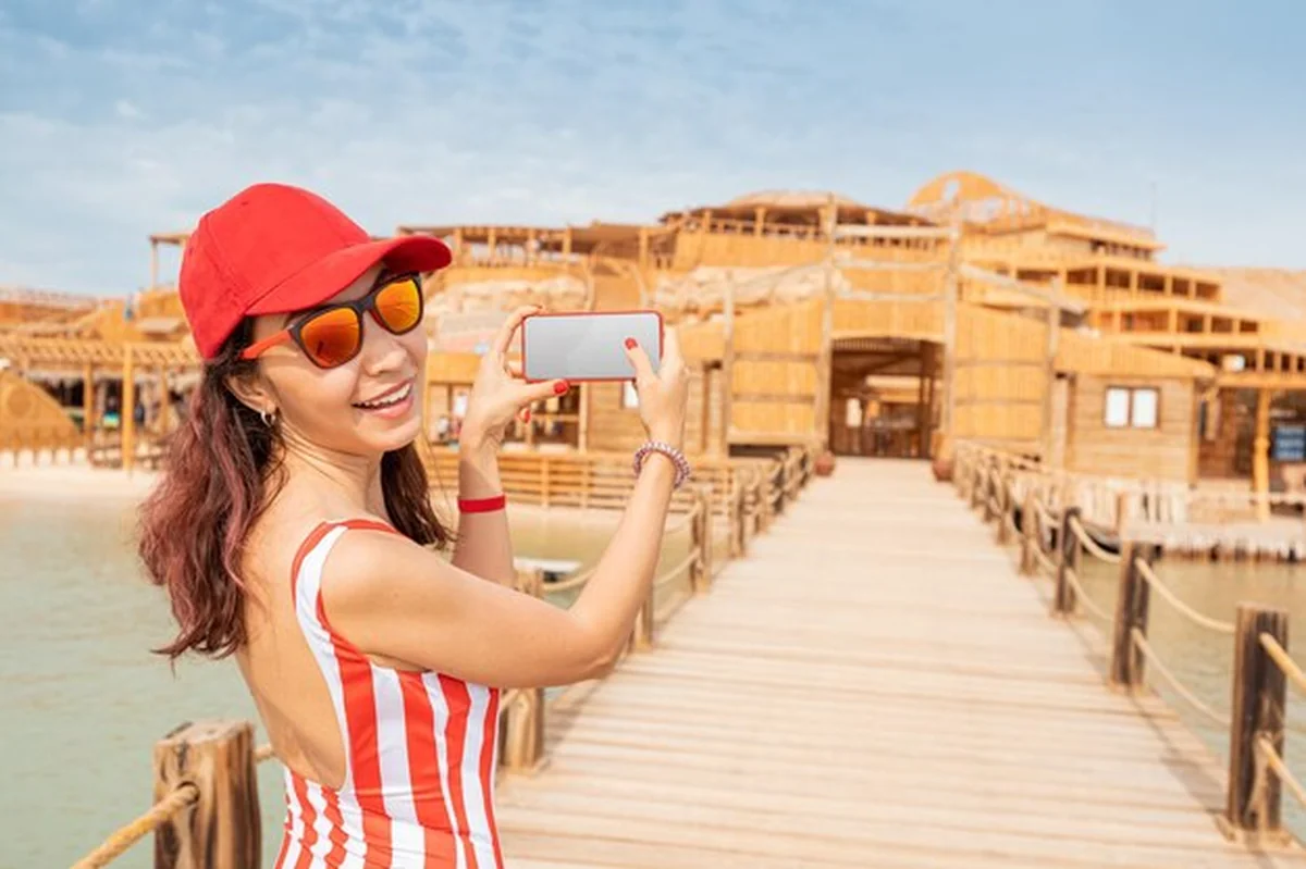 Szczęśliwa dziewczyna w kostiumie kąpielowym robi zdjęcia na smartfonie na kurorcie