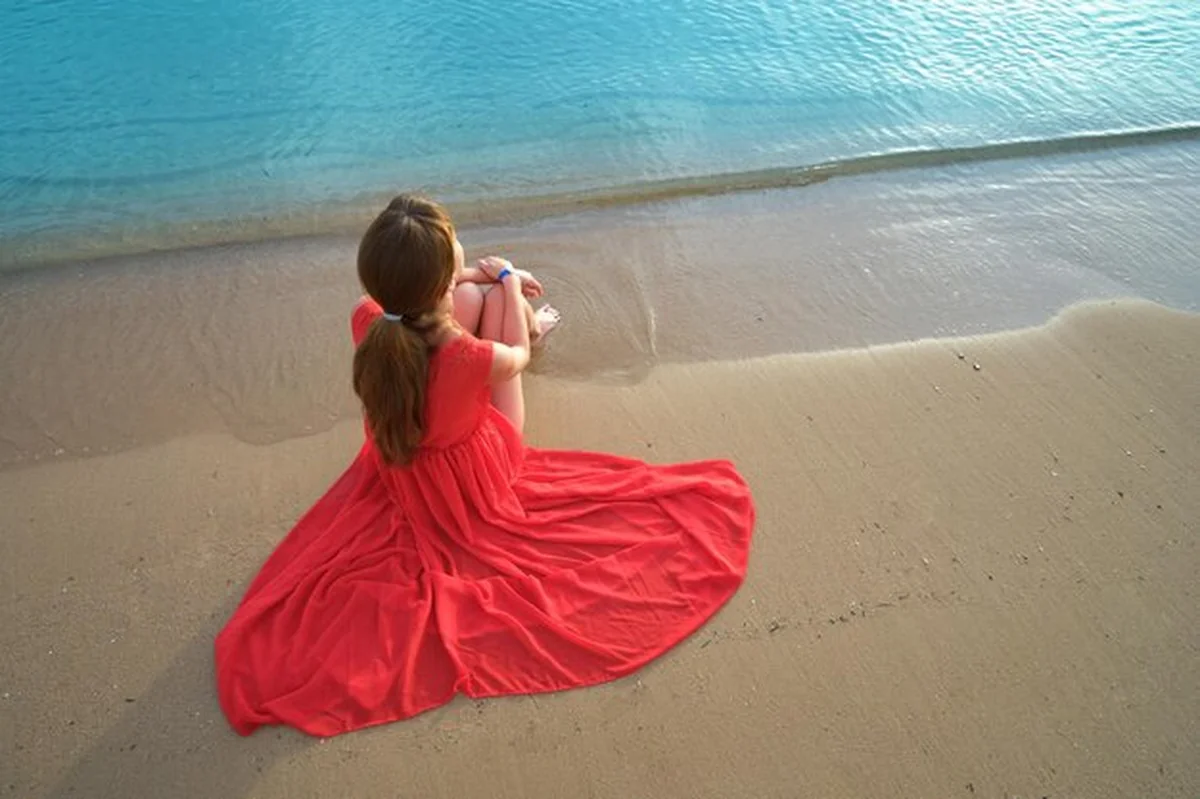 Młoda szczęśliwa kobieta w czerwonej sukience na plaży nad morzem