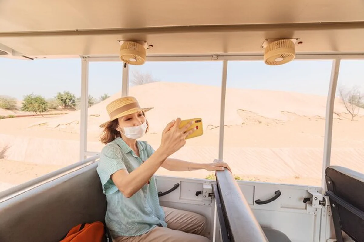 Turystka w masce medycznej, jedzie samochodem na safari i robi zdjęcie selfie na sawannie